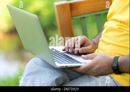 A man working and typing on laptop keyboard while sitting in the park Stock Photo