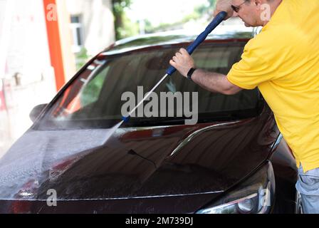 Car washing. Mature caucasian man cleaning automobile using high pressure jet water. Stock Photo