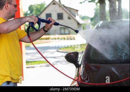 Car washing. Mature caucasian man cleaning automobile using high pressure jet water. Stock Photo