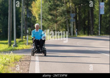 Smiling disabled old woman in a wheelchair on the highway Stock Photo
