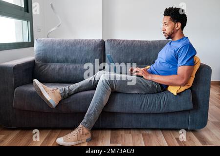 Man using a laptop while sitting on a sofa at home. Stock Photo