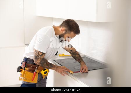 Man electrical repairs kitchen surface apartment. Installing hob in countertop. Man bought new kitchen furniture and appliances. Process installing an Stock Photo