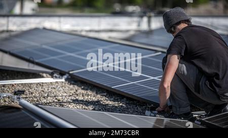 Male team engineers installing stand-alone solar photovoltaic panel system. Electricians mounting blue solar module on roof of company roof. Alternati Stock Photo