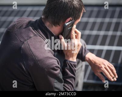 rooftop worker making phone calls with mobile phone during installation of solar panels Stock Photo