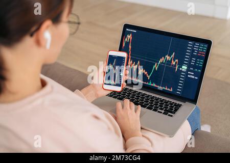 Close up of business woman trader investor analyst looking at financial stock market charts rate dynamic, using laptop and smartphone app for cryptocurrency digital analytics, buying cryptocurrency Stock Photo