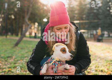 Woman pet owner walking dog jack russell terrier in funny clothes on street outdoors. Pet care concept Stock Photo