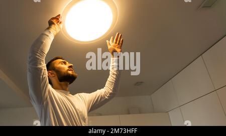 An electrician installs a chandelier on the ceiling. Hands of an electrician installing and connecting a lamp to a ceiling. Stock Photo