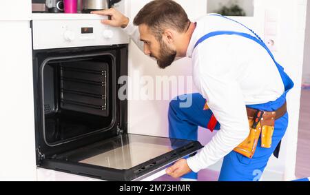 repairman examining oven with screwdriver in kitchen with tool case Stock Photo