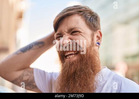 Young redhead man smiling confident touching head with hand at street Stock Photo