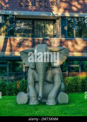 Cement gray elephant with big wide ears sculpture sitting on a grass in street Stock Photo