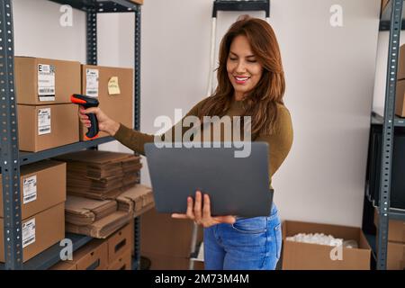 Young latin woman business worker scanning package using barcode reader at office Stock Photo