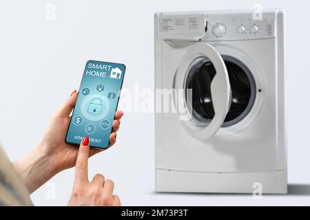Close-up Of Woman Hand Using Mobile Phone App To Operate Smart Washing Machine Stock Photo