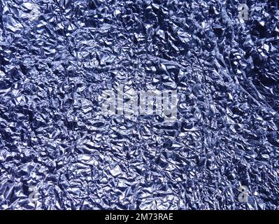 Crumpled aluminum foil background. Shiny and tinted faceted crinkled material. Stock Photo