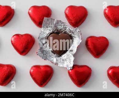 Love and relationship concept - close up of wrapped and unwrapped heart shape chocolate candies in red foil over white background Stock Photo