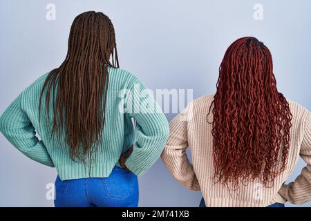 Two african woman standing over blue background standing backwards looking away with arms on body Stock Photo