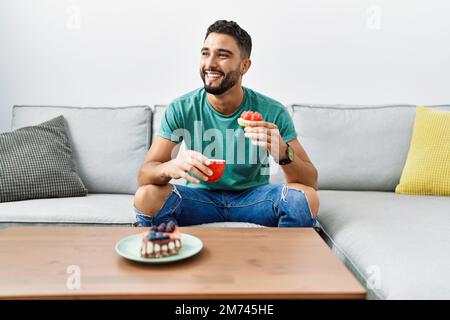 Young arab man having breakfast sitting on sofa at home Stock Photo