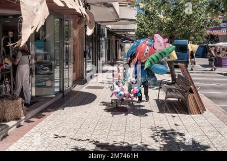 A man walks on the sidewalk between traffic selling a bunch of balloons during a festival or event in the town of Colindres, Cantabria, Spain Stock Photo