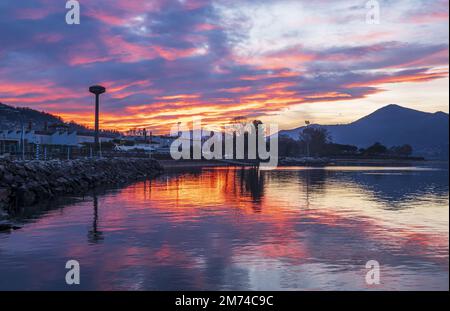 Beautiful colorful sunset with clouds and mountains reflecting on Lake Maggiore in Luino Stock Photo