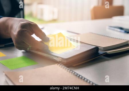 Close up shot of hands of man picking up sticking notes on notebook in office. Stock Photo