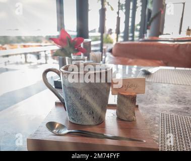 Coffee cup on wooden plate with sunrays in coffee shop and outdoor view. Stock Photo