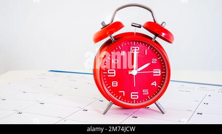 Red clock standing on calendar with white background behind Stock Photo