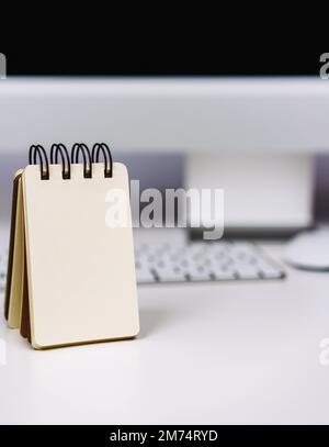 Notepad with blank page against personal computer on work desk. Stock Photo