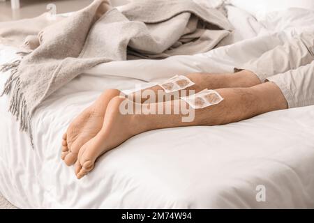 Ill man with mustard plasters on his legs lying in bedroom, closeup Stock Photo