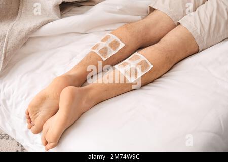 Ill man with mustard plasters on his legs lying in bedroom, closeup Stock Photo