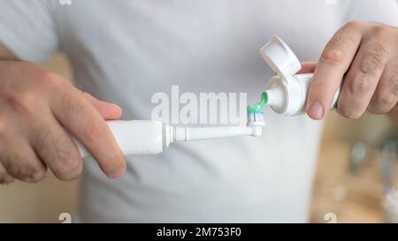 White man's hands pouring thootpaste into an electric toothbrush. Stock Photo