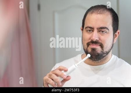 Young white man with a beard and a toothbrush, looking at the bathroom mirror and smiling. Stock Photo