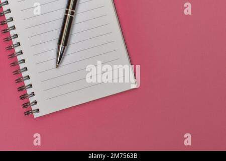 A notebook with a blank page and a pen resting on it on pink matte cardboard Stock Photo