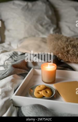 Cozy autumn composition with candle, cookies, notebook, and pencil in comfortable bed Stock Photo
