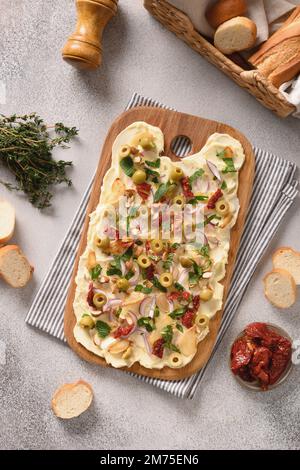 Homemade butterboard with onion, garlic, sun-dried tomatoes, herbs, crispy baguette on gray background. View from above. Vertical format. Trendy Butte Stock Photo