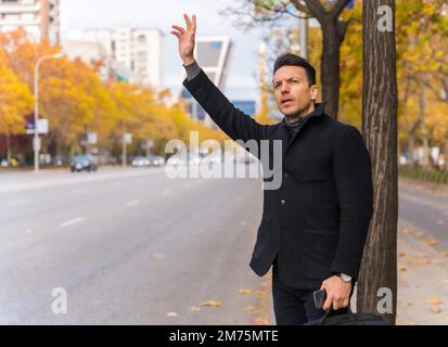 Middle-aged caucasian businessman hailing a taxi raising his hand to go to work Stock Photo