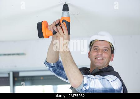 happy handyman using cordless drill against ceiling in new house Stock Photo
