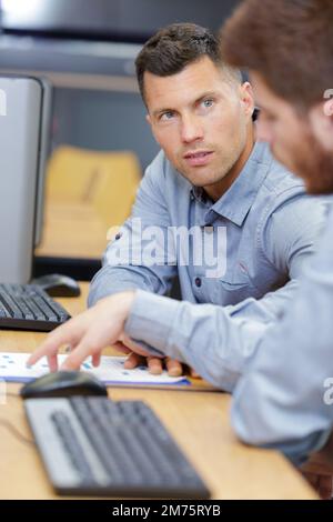two technicians in discussion sat at computer desk Stock Photo