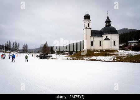 Seefeld, Austria - December 2022: Crosscrountry skiers (in motion blur) skiing near the Seekirchl chapel (also known as Heiligkreuzkirche) in Seefeld Stock Photo