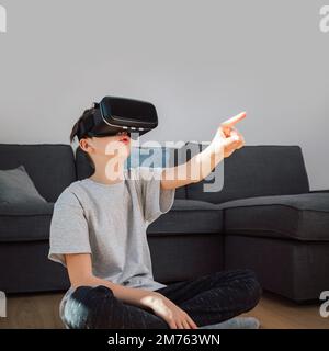 Caucasian school aged boy enjoying new technology at home, using VR goggles, and interacting with objects in a virtual world Stock Photo
