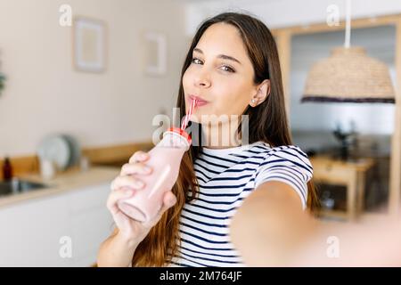 Joyful young adult woman taking selfie while drinking healthy fruit juice Stock Photo