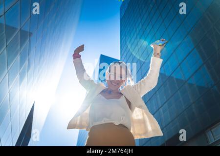 Happy businesswoman celebrating good news in front of business buildings. Stock Photo