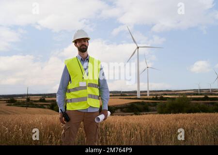 Working technical engineer looking at camera standing in a wind farm. Worker in a renewable energy Stock Photo