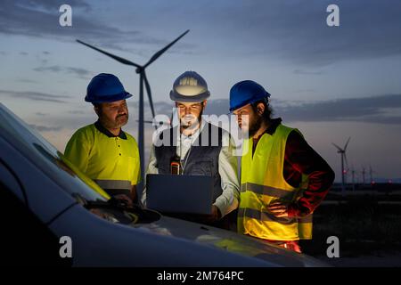 Group of engineers in discussed the plan for the maintenance of wind turbines working with a laptop Stock Photo
