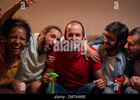 Joyful football fans cheering for favorite team while watching match on TV sitting on sofa at home Stock Photo