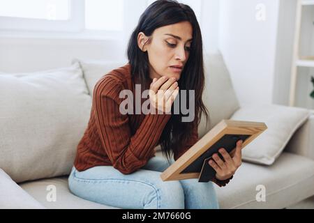 The woman looks sadly at the picture frames in her hands and with memories, a state of depression and loss of a person Stock Photo