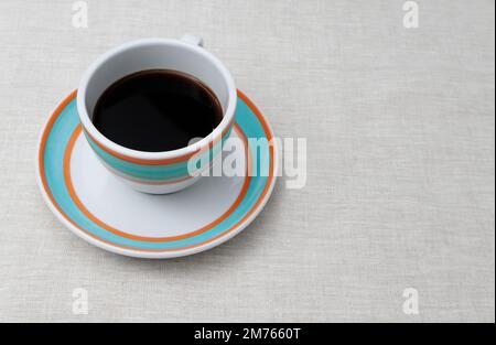 Colorful cup of black coffee is placed on the saucer. Both, the cup and the saucer are white with orange and aqua colored rings drawn on them. Stock Photo
