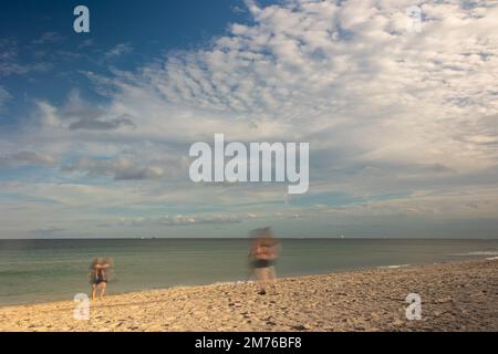 Motion blur of two women walking on a beach in Fort Lauderdale, under a pretty cloudscape. Stock Photo