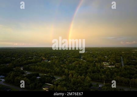 Colorful round rainbow over rural town suburbs against blue evening sky after heavy thunderstorm. Stock Photo