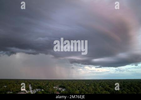 Landscape of dark ominous clouds forming on stormy sky during heavy thunderstorm over rural town area at sunset Stock Photo