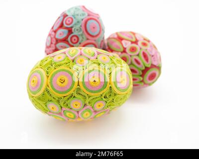 Close up of three quill art Easter eggs against a white background. The eggs are lime green, pink, yellow, and fuchsia. Stock Photo