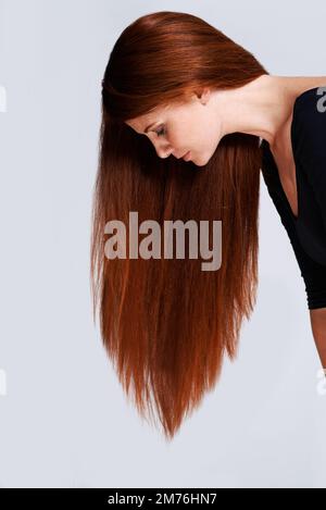 The profile of healthy hair. Studio shot of a young woman with beautiful red hair posing against a gray background. Stock Photo